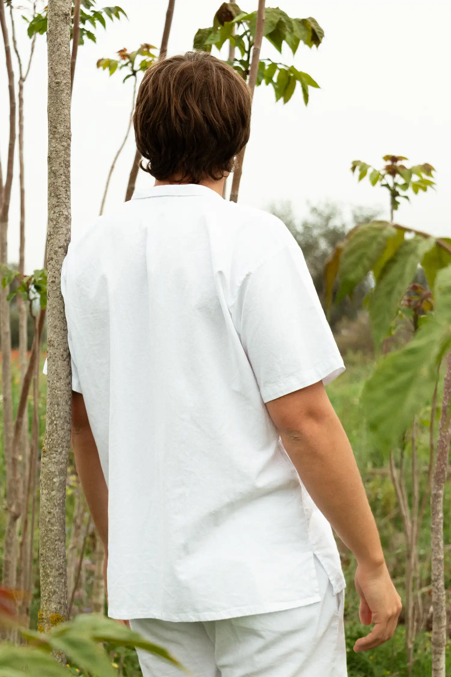 Modelo masculino con camisa ibicenca de hombre blanca entre vegetación vista trasera.